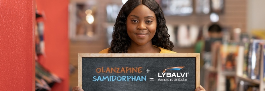 Woman in a bookstore smiling and holding a sign that shows the components of LYBALVI® (olanzapine and samidorphan)