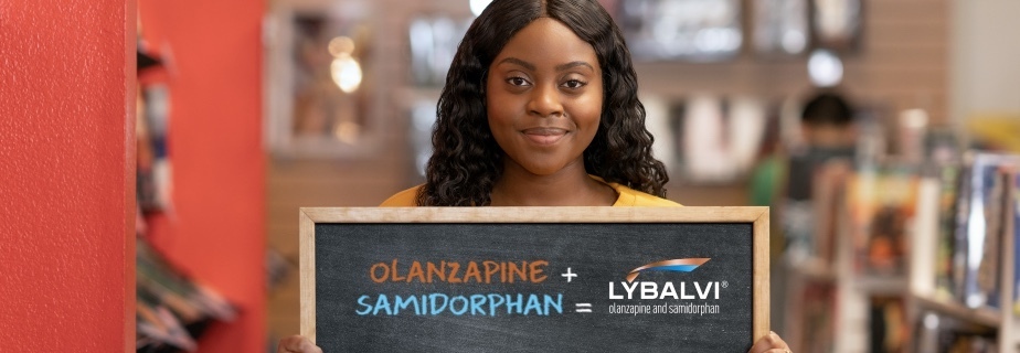 Review the efficacy and safety of LYBALVI® (olanzapine and samidorphan) Woman in a bookstore smiling and holding a sign that shows the components of LYBALVI® (olanzapine and samidorphan)