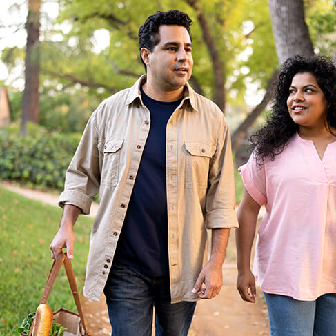 Man and woman walking in a park together, carrying a bag of groceries